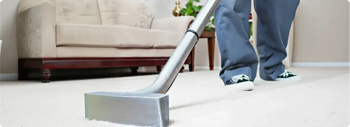 Carpet cleaning technician using a hot-water extraction wand on a light-colored carpet in a living room, Eugene, OR.